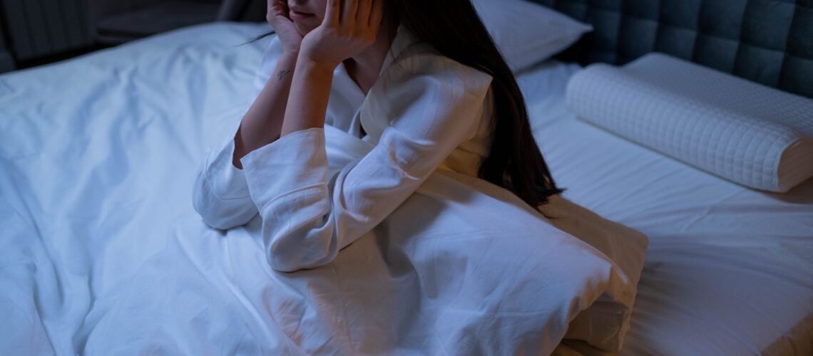 An Asian woman in bed at night, experiencing insomnia and loneliness, deep in thought.