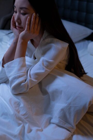 An Asian woman in bed at night, experiencing insomnia and loneliness, deep in thought.
