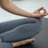 Crop unrecognizable person in sportswear sitting on floor and meditating in lotus pose during yoga session