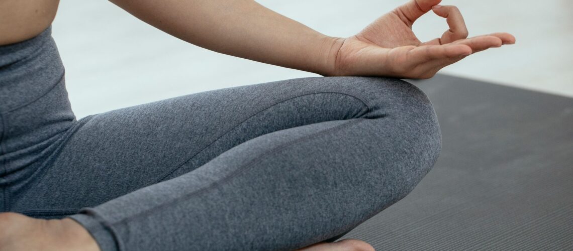 Crop unrecognizable person in sportswear sitting on floor and meditating in lotus pose during yoga session