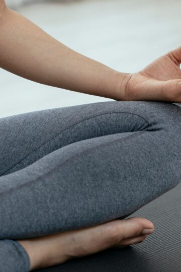 Crop unrecognizable person in sportswear sitting on floor and meditating in lotus pose during yoga session