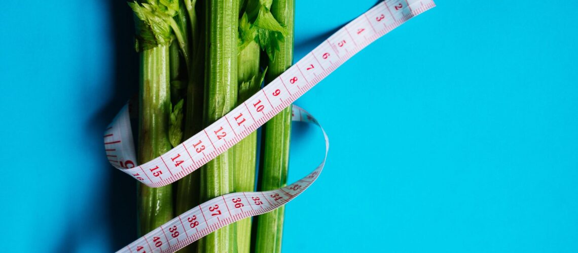 Close-up of celery stalks wrapped with measuring tape on a vibrant blue background, symbolizing health and diet.