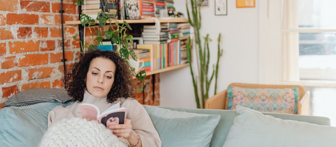 Woman relaxing with a book on a cozy sofa in a home library setting.