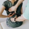 From above of crop faceless slim female patient sitting on examination couch and indicating osteopath in uniform pain spot on back in clinic