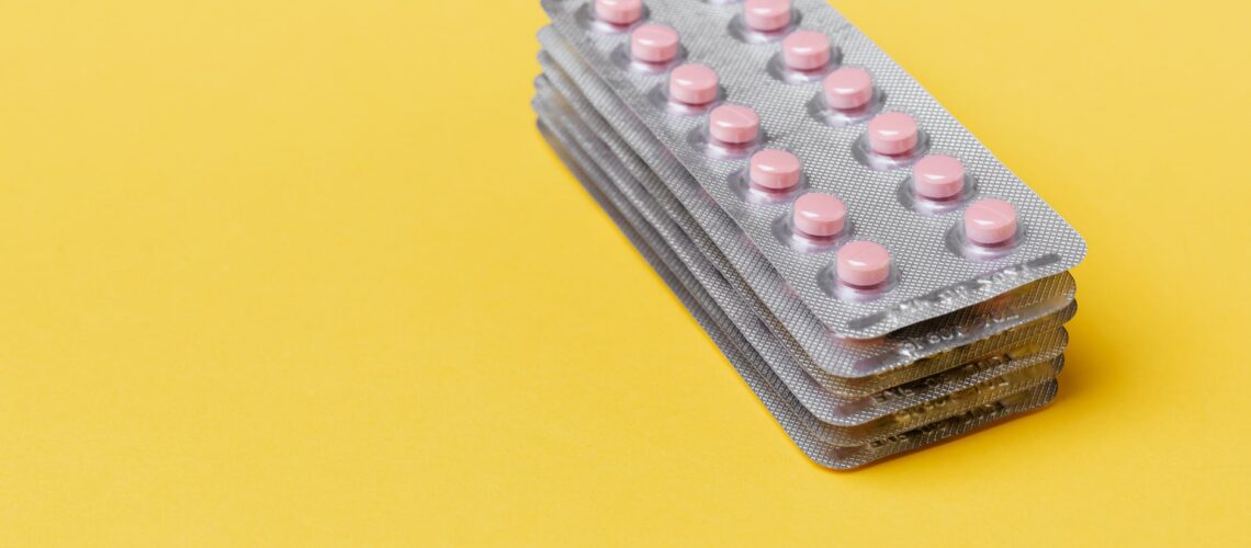 From above set of small round pink pills packed in blisters on top of each other on yellow surface