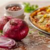 Red onions and fresh tomatoes arranged near a delicious pizza, ideal for food photography.