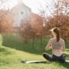 A woman meditating outdoors on a yoga mat in a serene park during a sunny day.