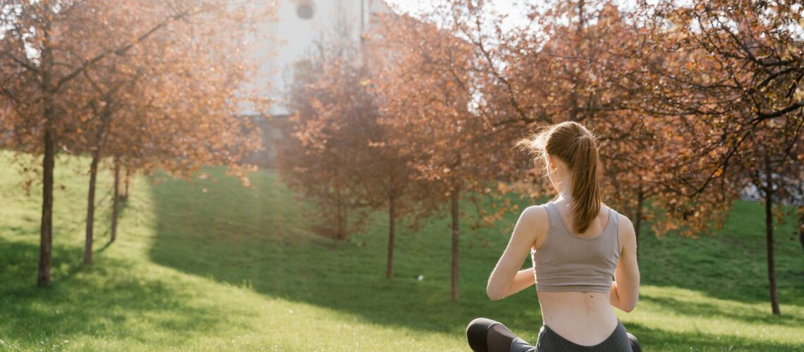 A woman meditating outdoors on a yoga mat in a serene park during a sunny day.