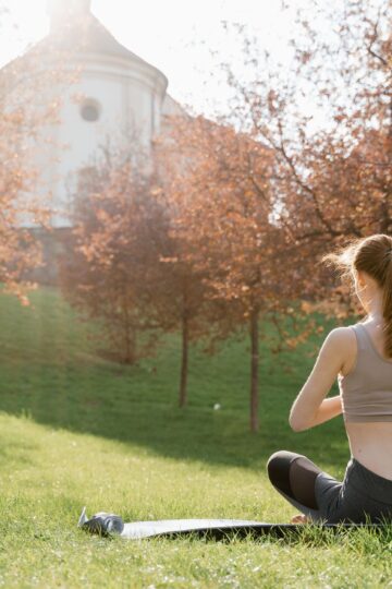 A woman meditating outdoors on a yoga mat in a serene park during a sunny day.