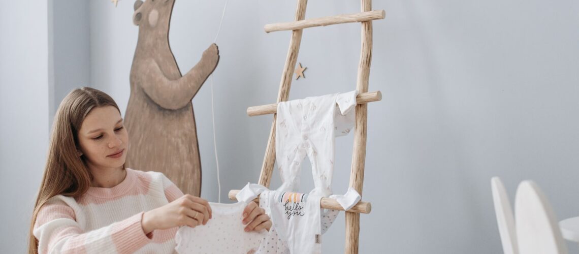 Pregnant woman arranging baby clothes in serene indoor setting with playful decor.