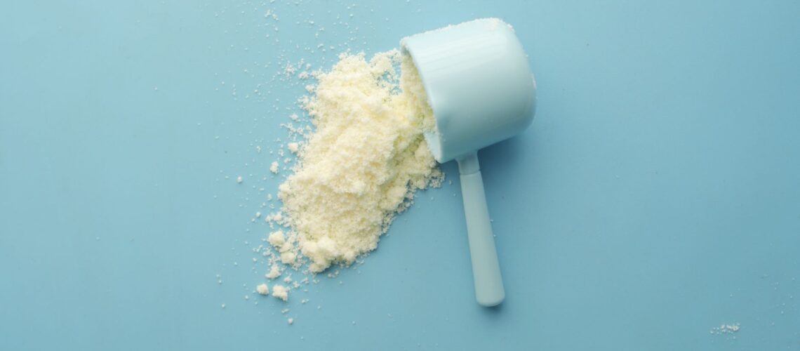 White powder spilled from a scoop on bright blue background. Clean and minimalistic food photo.