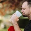 Adult man savoring a protein shake in a peaceful outdoor setting during the day.