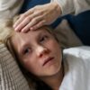 Young child lying down with a hand checking for fever, indicating illness or flu symptoms.
