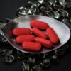 A detailed close-up of red pills on a spoon surrounded by transparent capsules.