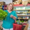 Smiling elderly woman with groceries in a store, showing fresh produce.