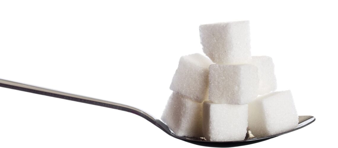 Close-up of sugar cubes stacked on a spoon against a white background, highlighting simplicity and sweetness.