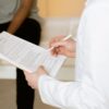 Healthcare professional reviews medical form during patient consultation in a clinic setting.