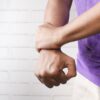 Close-up of a person holding their wrist in pain against a brick wall background.