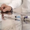 A veterinarian in a clinic setting preparing syringes and vaccine vials on a reflective surface.