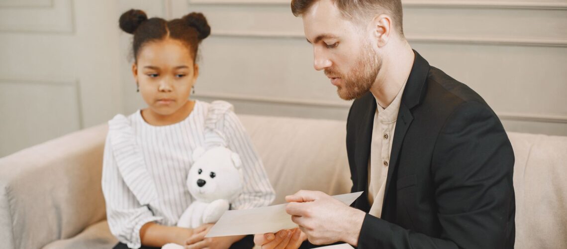 A child holding a plush toy listens to a man in a therapy session.