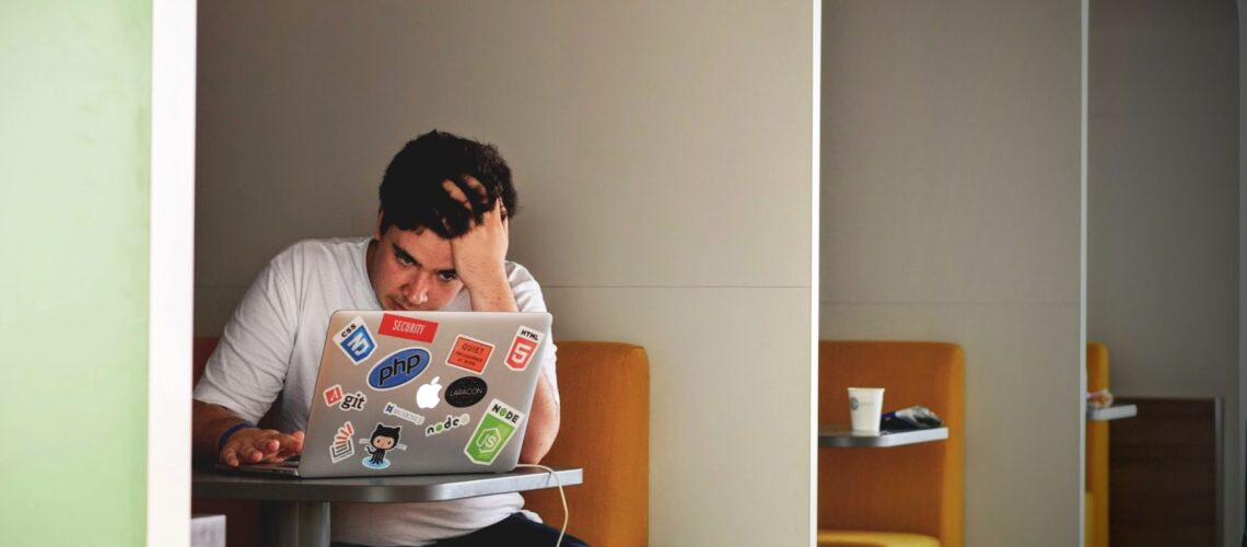 Man showing stress and frustration while working remotely on a laptop indoors.