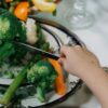 A child uses a knife to cut fresh broccoli and vegetables on a plate. Healthy eating concept.