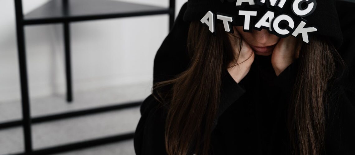 A woman sitting with 'PANIC ATTACK' on her hood, showing anxiety indoors.