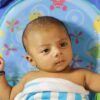 Cute baby wrapped in a striped towel resting in a colorful chair indoors.