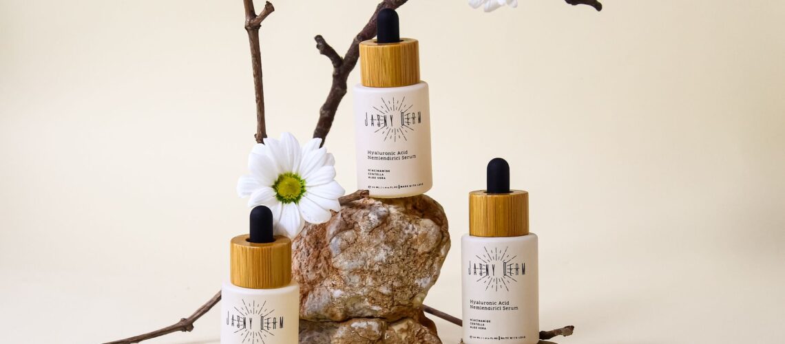 Organic hyaluronic acid serum bottles with floral and stone arrangement on neutral background.