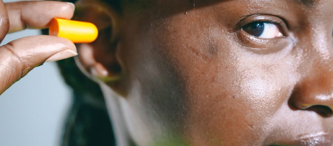 A close-up image of a woman inserting an earplug, wearing safety gear.