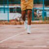 Close-up of a man's legs running on an outdoor basketball court, wearing yellow shorts and sneakers.