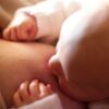 Intimate close-up of a newborn baby breastfeeding, captured in warm, softly lit setting.