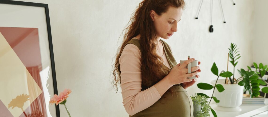 Cozy indoor scene of a pregnant woman holding a cup surrounded by plants.