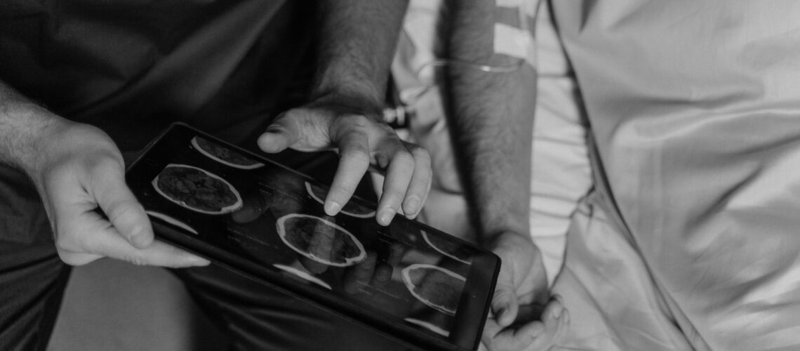 Medical professional reviews patient's CT scans on a digital tablet in grayscale.