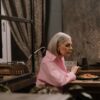 Elderly woman in a pink shirt enjoying dinner alone by candlelight at home.