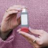 Female hands holding an asthma inhaler with a pink sweater background.