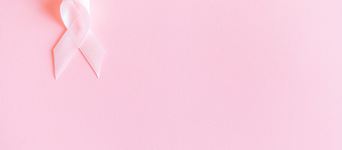 A pink ribbon on a soft pink background symbolizing breast cancer awareness and solidarity.