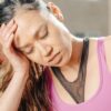 A woman in a purple top experiencing a headache under bright sunlight.