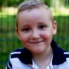 Happy young boy smiling confidently outdoors against a blurred background.