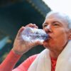 Elderly man drinking water post-exercise with towel around neck, promoting healthy lifestyle.