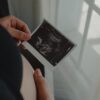 Pregnant woman holding an ultrasound scan of her unborn child, symbolizing motherhood.