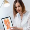 Woman in white blouse using tablet to explain facial anatomy in clinic.
