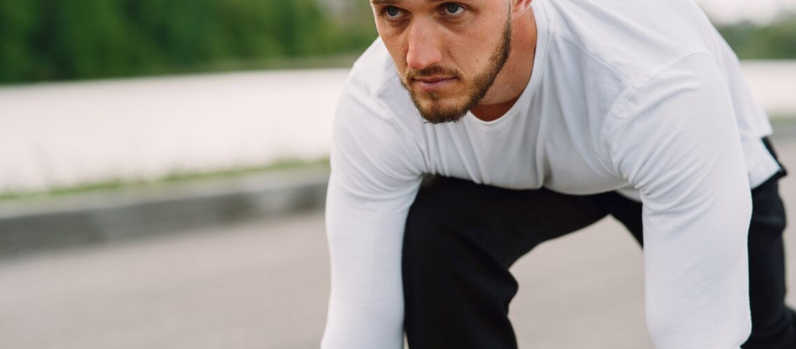 Athletic man in sportswear on a starting line, ready for a sprint workout outdoors.