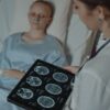 A doctor analyzes brain scans on a digital tablet beside a patient in a hospital bed.