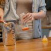 A parent prepares a baby bottle with formula on a wooden table in a cozy kitchen setting.