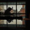 Silhouette of a person in a hoodie using a smartphone inside a café with street view.