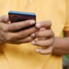 Close-up of a person in an orange shirt using a smartphone outdoors.