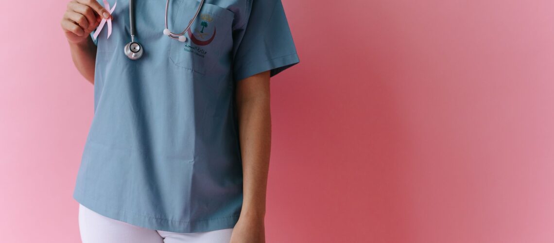 A medical professional holding a pink ribbon for breast cancer awareness against a pink background.