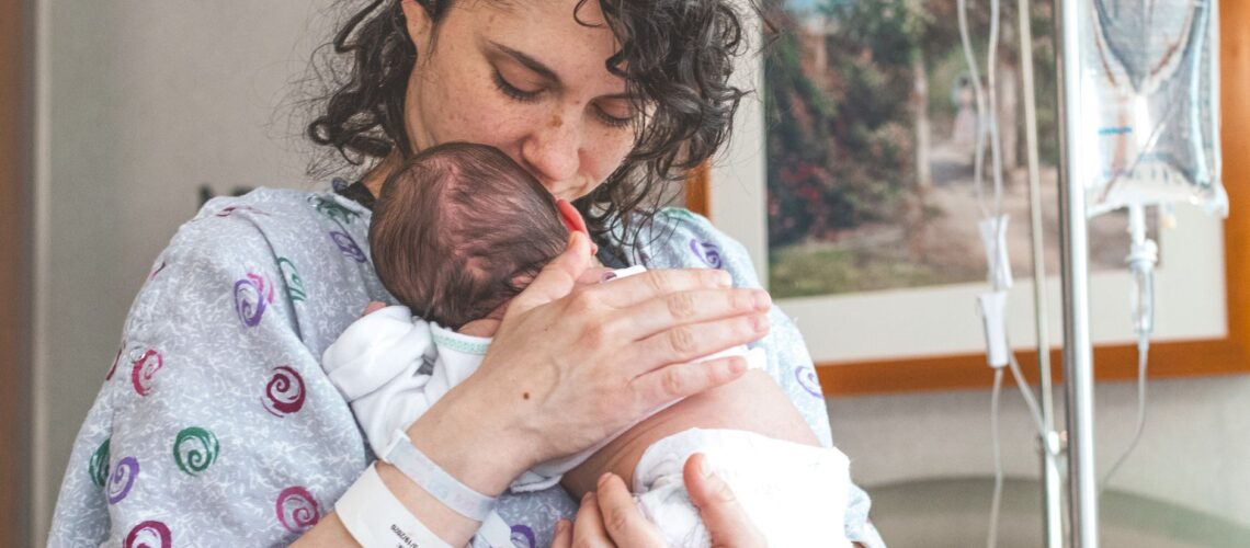 Mother gently holding newborn baby in hospital setting, showcasing warmth and love.