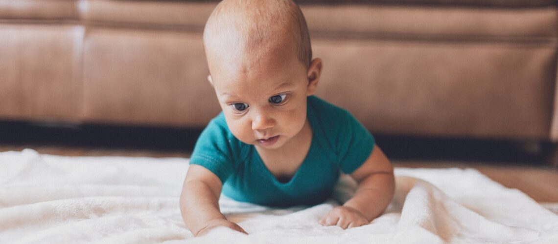 Cute baby crawling on a soft white blanket indoors, showcasing innocence and playfulness.